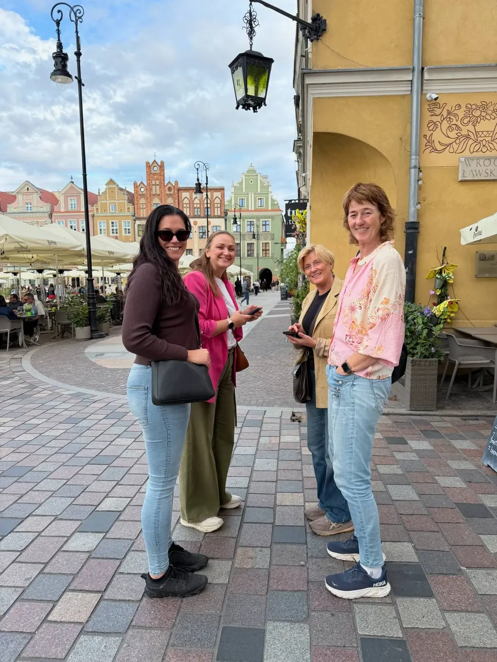 Fire kolleger fra Skya smiler på et torg i en gammel bydel